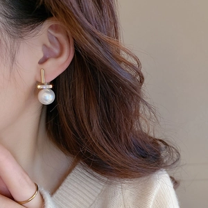 Detailed view of elegant gold pearl earrings with crystal inlay on a female model