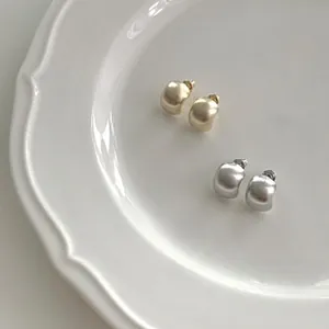 Detail view of chunky dome earrings in matte gold and silver on a white ceramic plate