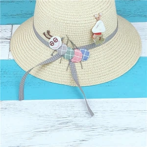 Flat lay of hand-woven straw hat with colorful caterpillar decor on striped wood background