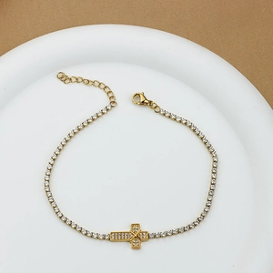 Elegant gold-plated cross bracelet with cubic zirconia on a white ceramic display