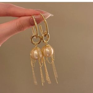 Detailed close-up of golden tassel drop earrings with pearls held by a hand
