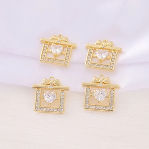 Macro shot of four golden gift box pendants with heart-shaped crystal on white silk