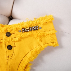 Dettaglio degli shorts di jeans gialli con strass brillanti e orlo con frange a vivo