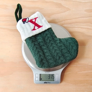 Detail of green cable knit Christmas stocking showing weight of 31.5g on a scale