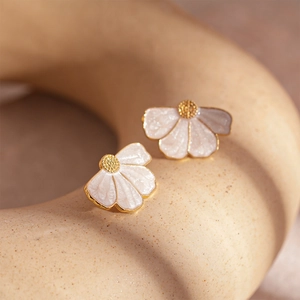 Macro shot of elegant fan-shaped floral stud earrings with white enamel and gold edges