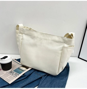 Detail of cream white canvas tote bag side pocket with broad strap on blue denim background