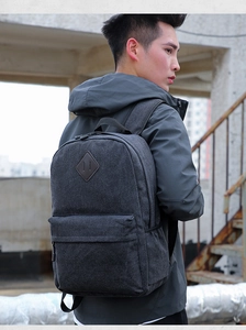 Side view of dark grey canvas backpack showing the diamond-shaped leather patch and straps