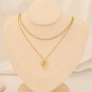 Detail of a gold double-layer necklace featuring a snake chain and a 3D heart pendant