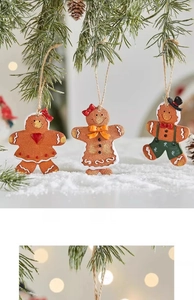 Three gingerbread man ornaments hanging on pine branches over a snowy background