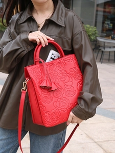 Borsa a mano rossa in pelle goffrata con rose e nappina indossata da modella in stile street
