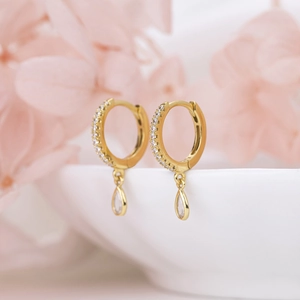Elegant gold hoop earrings with sparkling diamonds and teardrop pendant on white ceramic