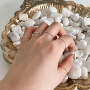Detailed view of layered S925 sterling silver twist rings on hand with elegant pebbles