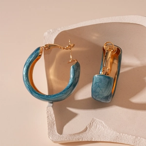 Detail of teal resin wide hoop earrings with gold metal interior on minimalist background