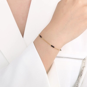 Bracelet chaîne dorée chic avec accents cylindriques noirs porté au poignet d'un mannequin