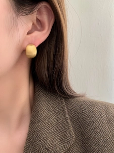 Close-up detail of a minimalist geometric matte gold stud earring worn by a model