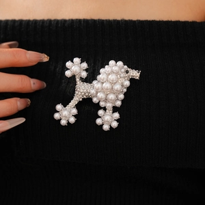 Close-up of a vintage pearl poodle brooch with rhinestones on a black striped knit sweater