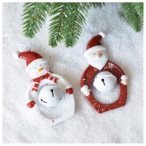 Close-up of Santa and snowman resin bell ornaments with white ribbon hanging on pine branch