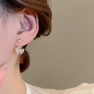 Close-up of a silver bow earring with sparkling zircon stones on a female model