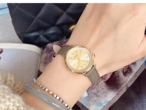 Detail of luxury woman watch with crystal bezel, gold dial and grey leather strap