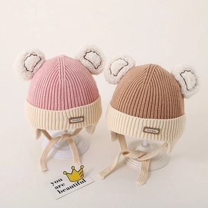 Close-up of knit baby earflap hats with plush bear ears and First Day leather tag