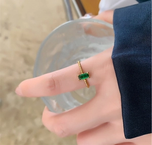 Close-up of twisted gold ring with emerald-cut green stone worn by model on a glass