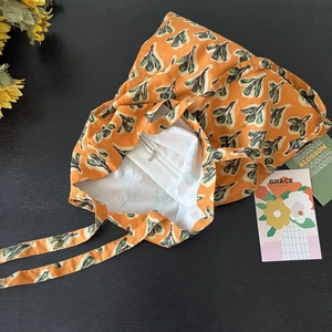 Detail of printed cotton tote with orange base, green leaf patterns, and internal zip pocket