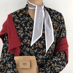 Detail of grey and white silk scarf tied on neck with LOVE NEVER FAILS PARIS text