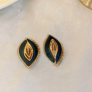 Detail of vintage gold-rimmed earrings with green and blue enamel leaf motif on silk