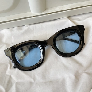 Detail of polygonal black sunglasses with light blue lenses on white fabric backdrop