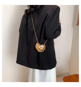 Detail view of heart-shaped gold metallic handbag with pearl chain strap on model shoulder
