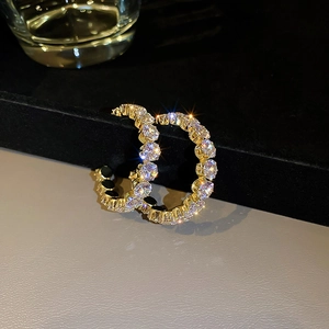 Macro shot of gold C-shaped earrings with shimmering clear rhinestones on black background
