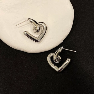 Macro detail of silver-tone twisted heart earrings on a minimalist black and white background