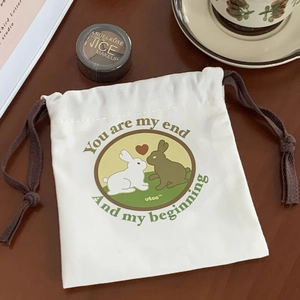 Close-up of white canvas drawstring bag with cute rabbit illustration on a wooden table