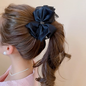 Dettaglio di una pinza per capelli con fiocco nero e strass lucidi su una coda