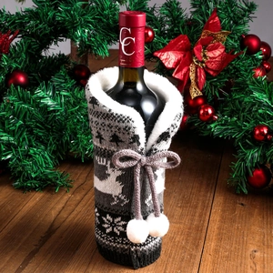 Knitted Christmas wine bottle cover with reindeer pattern and pompom on wooden table