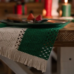 Forest green and cream cotton woven placemat with festive tassels on a wooden table