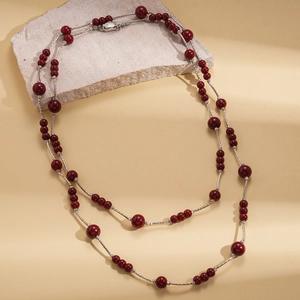 Detail of double-layer long necklace with deep red beads and silver rope chains on stone