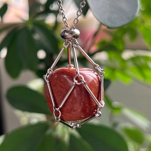 Macro shot of red goldstone pendant in a silver woven wire mesh necklace cage