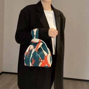 Detail of colorful knitted tote bag with abstract patterns worn by a model in casual blazer