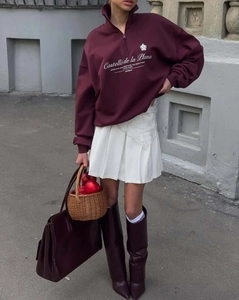 Outdoor shot of burgundy half-zip sweatshirt paired with white pleated skirt and tall boots