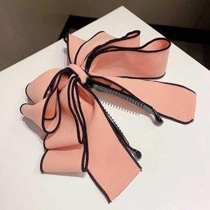 Detail of pink fabric bow hair clip with black trim on a minimalist white surface