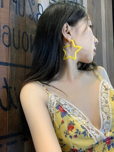 Detail of a large yellow star-shaped acrylic earring worn by a model in a retro style