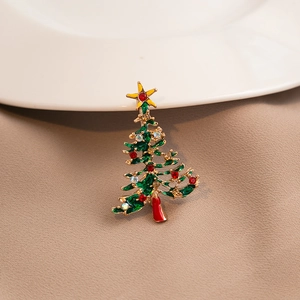 Detailed view of a green Christmas tree brooch with colorful gems on a beige fabric background