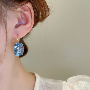 Macro shot of a light blue cushion-cut gemstone earring with a golden lever-back hook