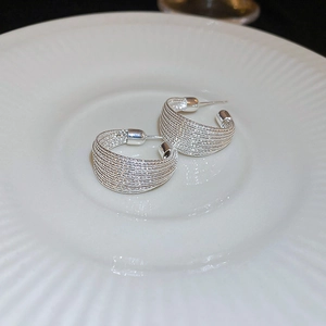 Detail of silver twisted C-shape hoop earrings with layered lines on a textured ceramic plate