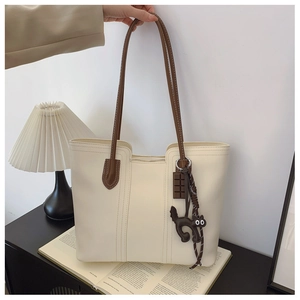 Detail of cream tote bag with brown straps and cute cat charm on a wooden table