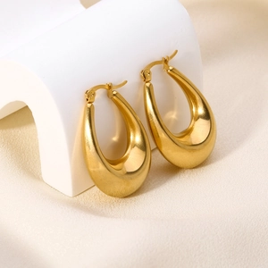Close-up of polished 18K gold-plated teardrop hoop earrings on a minimalist display stand