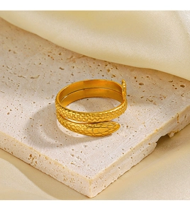 Close-up of gold snake ring with detailed scales on textured stone and silk background