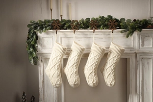 Set of four cream cable knit Christmas stockings hanging on a white fireplace mantel
