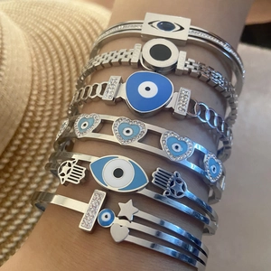Nahaufnahme gestapelter silberner Evil Eye und Hamsa Hand Armbänder mit Emaille